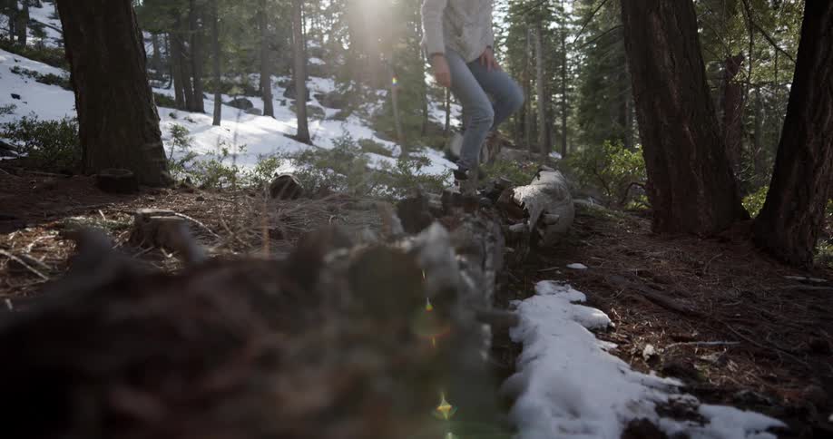 Woman wearing cold weather gear and sunglasses hikes across snow covered ground in forest