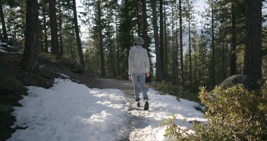 A woman walking in a forest on a trail that has snow on it