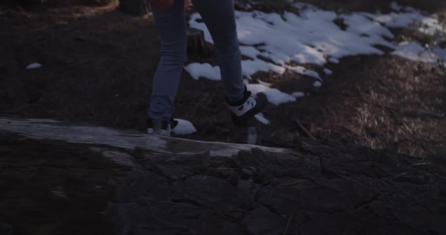 A woman walks through a woodland with patches of snow on the ground during the day