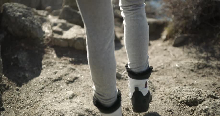Legs walk down a rocky slope toward water