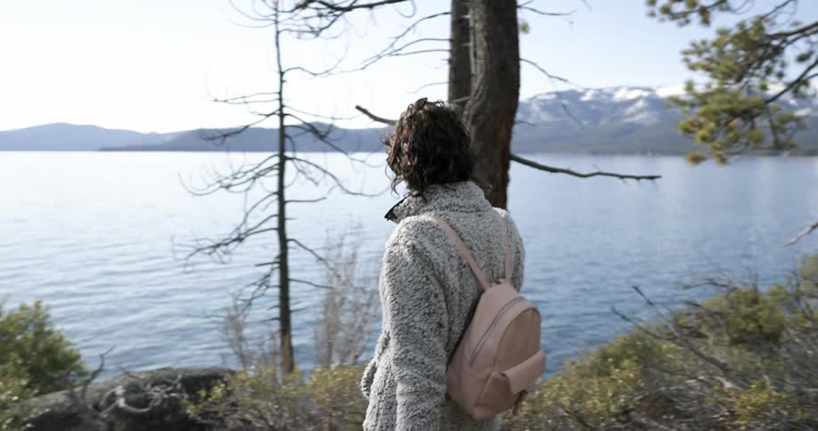 A woman walks through a forest and down toward a lake to take in the view of nearby mountains