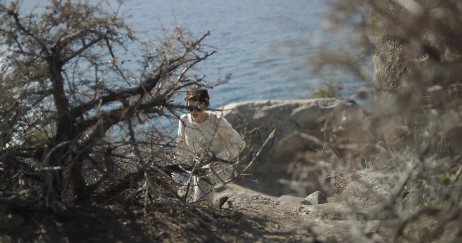 Woman wearing sunglasses hikes on a trail throught the rocks in the mountain near a lake