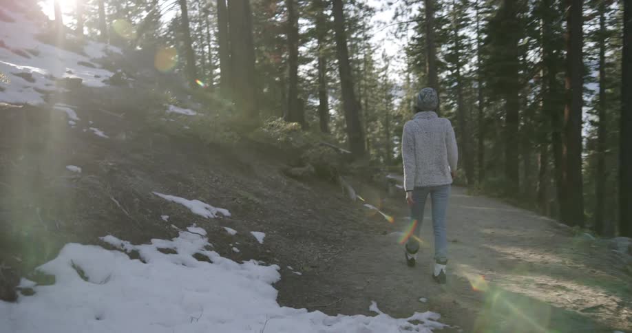 Woman walks along partly snow covered ground through forest