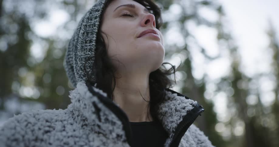 A sad woman standing in the forest wearing winter clothes takes sunglasses out