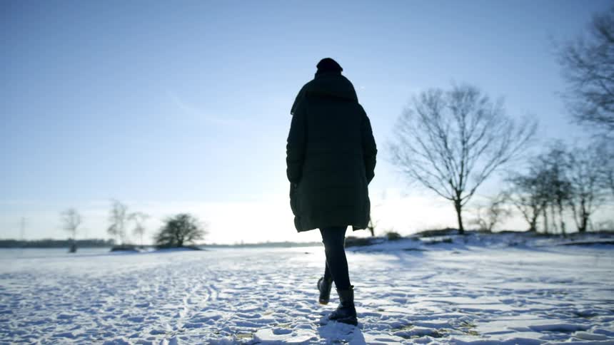 A person in a long coat walking outside on snow on a sunny winter day