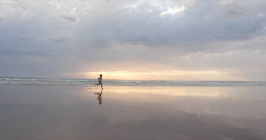 A person is jogging on the beach at dusk