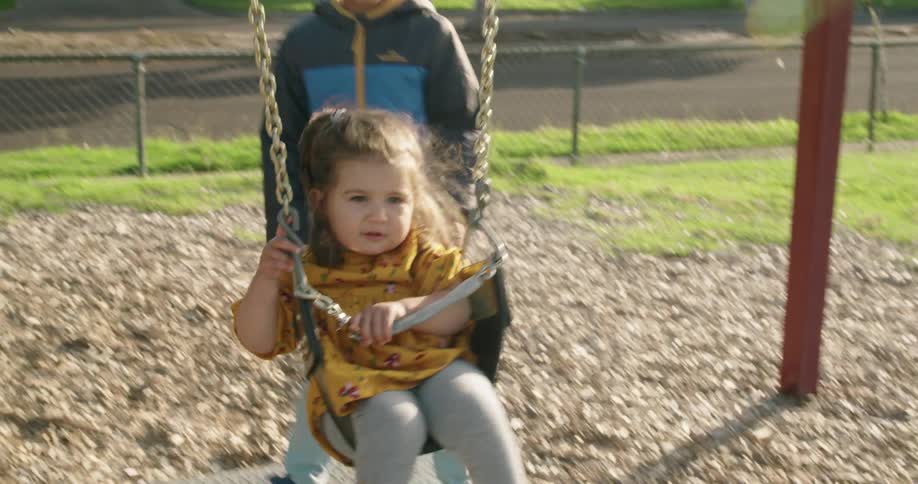 A boy pushes a girl on the swing