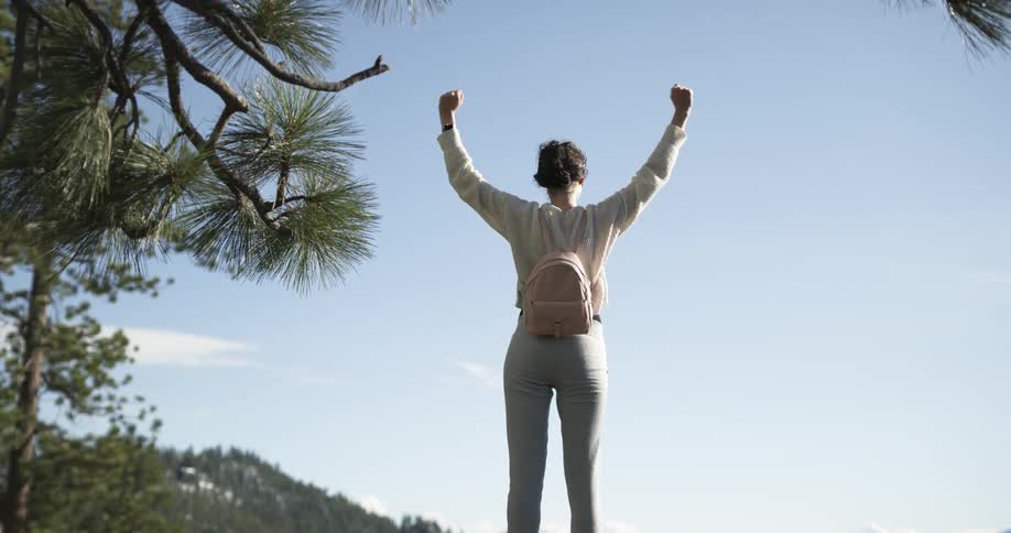 A woman raising her arms in celebration while hiking alone in mountains