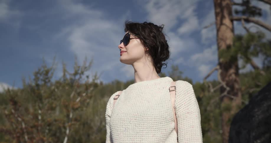 Young woman wearing sunglasses looking at the horizon standing on the forest in the mountain