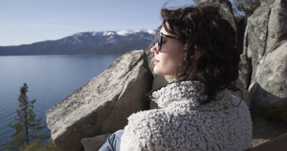 A woman sits on a chair next to large boulders at a canyon and takes in the view of the lake below
