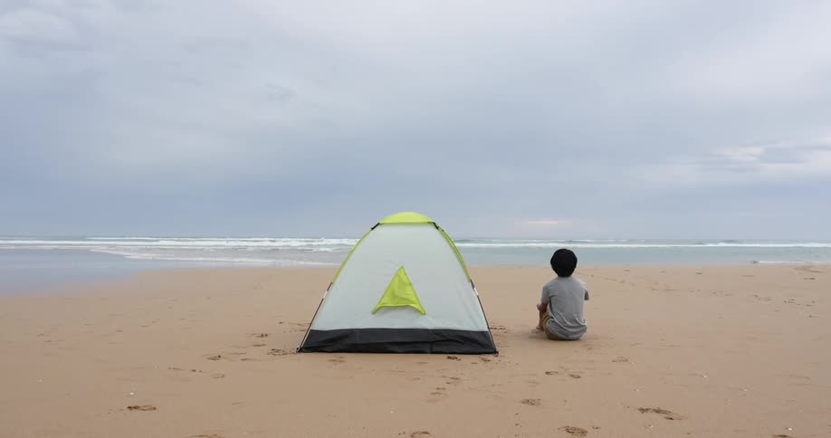 A child sitting next to a tent at the beach