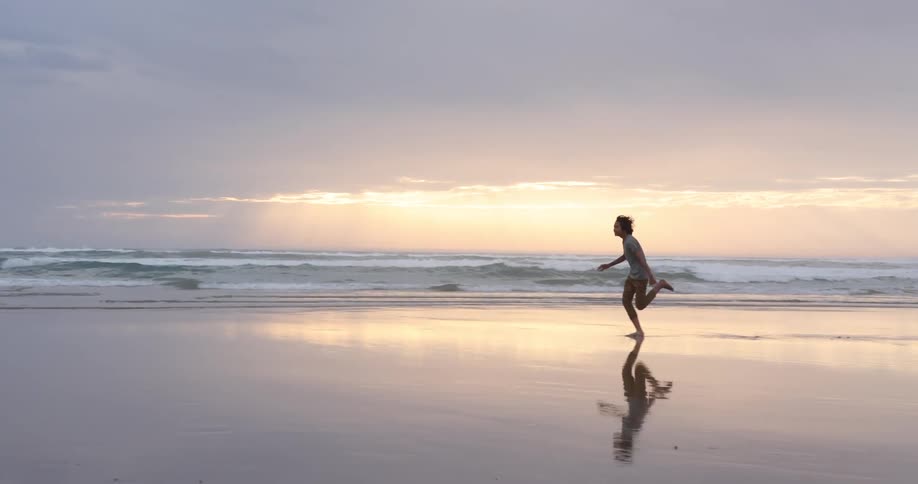 A person running on a beach with the ocean sky and clouds in the background