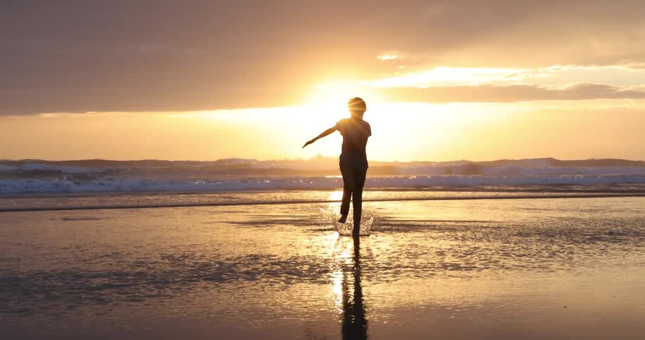 Silhouette of a person running barefoot over the wet sand near the ocean at sunset