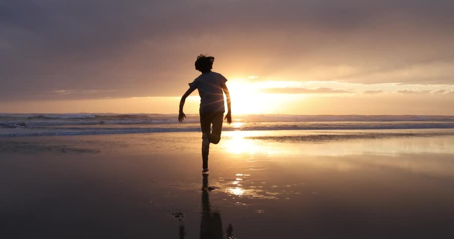 A boy is running towards the water on the beach