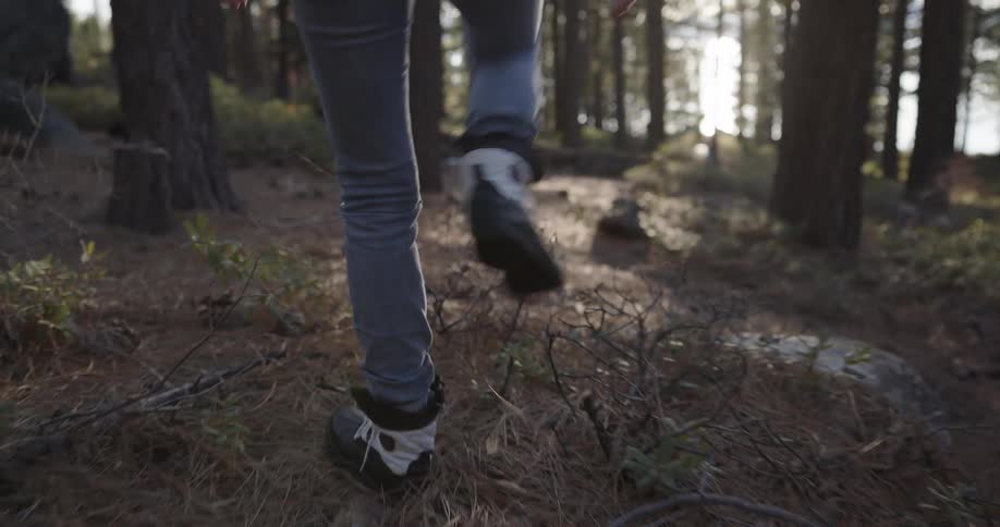 A woman wearing white boots and jeans walking on the forest at sunset
