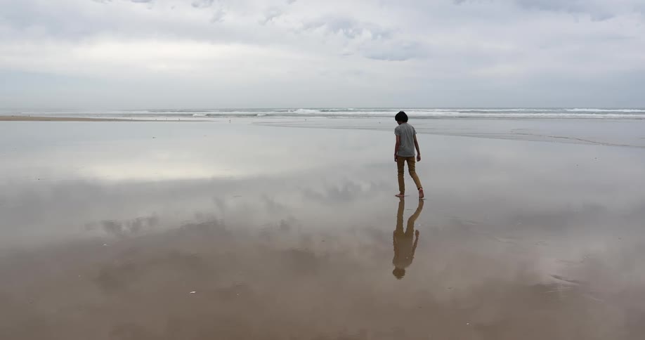 A preteen boy walks on the beach where the sand meets the ocean