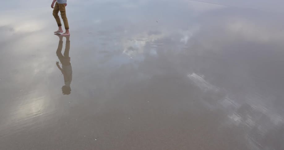 Man walks through very shallow water that reflects him and the sky