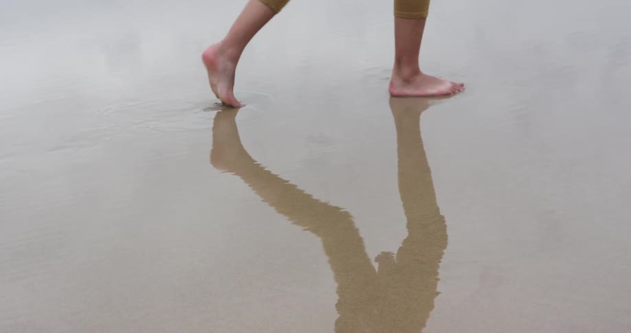 A person walking on a beach on sand wet with water