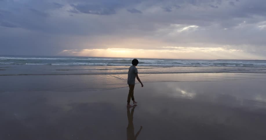 A person is walking in the sand at sunset