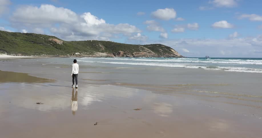 A person walks along the wet sands of a beach on a sunny day