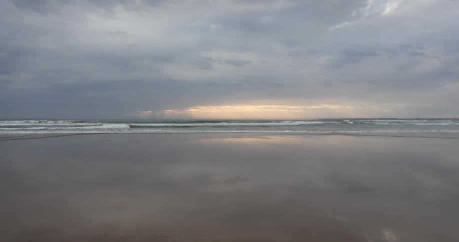 Dense clouds loom as the tide washes onto the beach at sunrise
