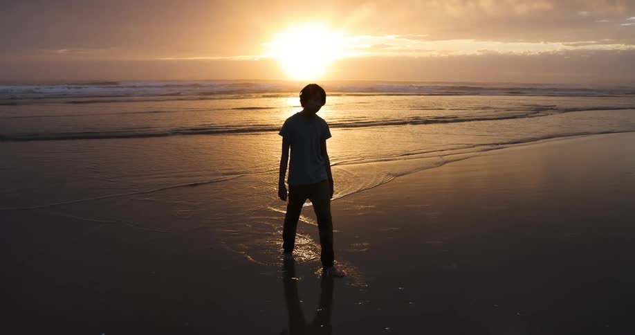 A preteen boy wades in the ocean at dusk