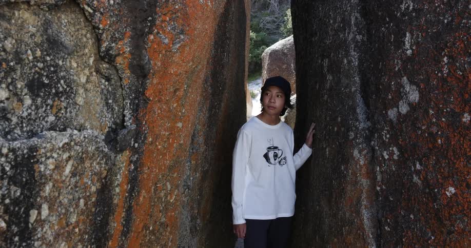 A teenage boy walks between two large rock formations