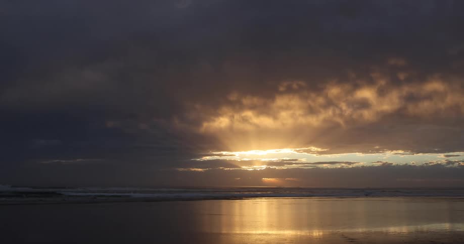 The sun shines through dense clouds over the ocean