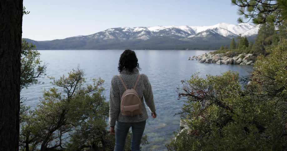 A woman hiking alone near a lake with snowy mountains in the distance