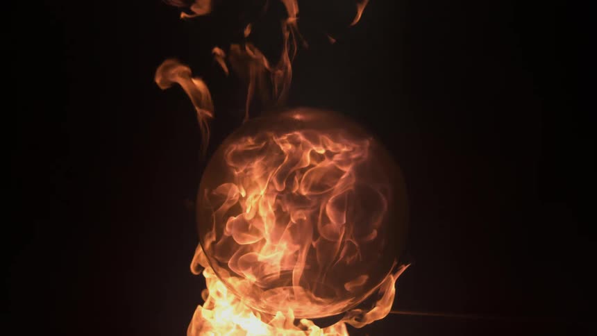 Orange flames surging inside and outside a glass ball on a black background