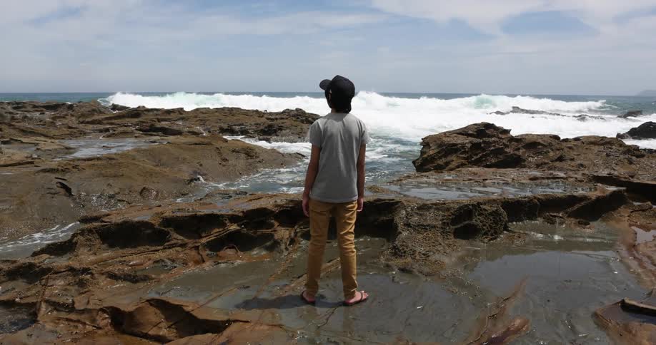 A person is standing in the water looking at the ocean