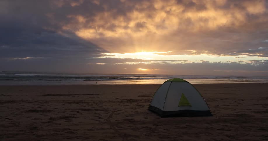 A white tent is set up on the beach for camping