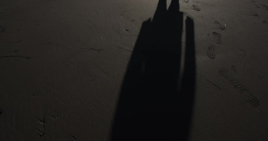 Long shadow of a person walking over wet sand at night