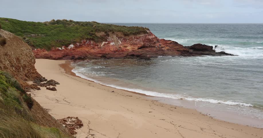 Ocean waves roll into a sandy beach in a small bay during the day