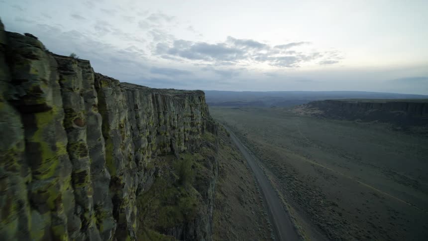 Flying next to a a sheer cliff above a lonely and empty road in a desert landscape