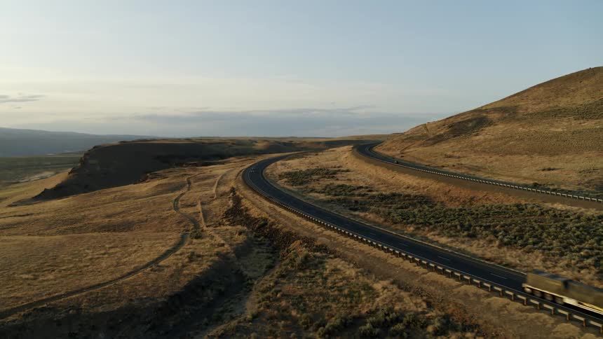 A semi truck rounds a bend along an interstate highway on a golden hillside