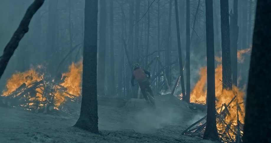 A person wearing a helmet rides a mountain bike through a smokey burning forest