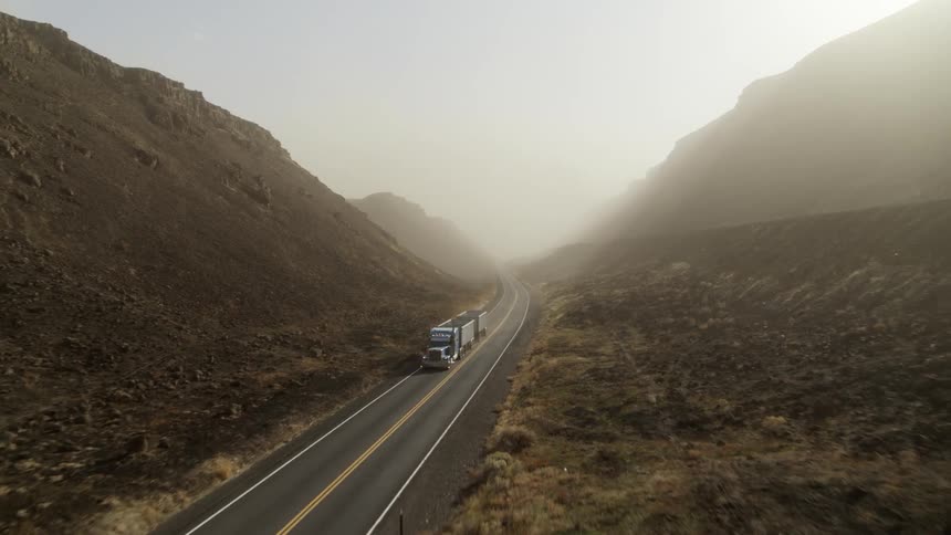 A double trailer semi truck traveling down a canyon road and out of frame