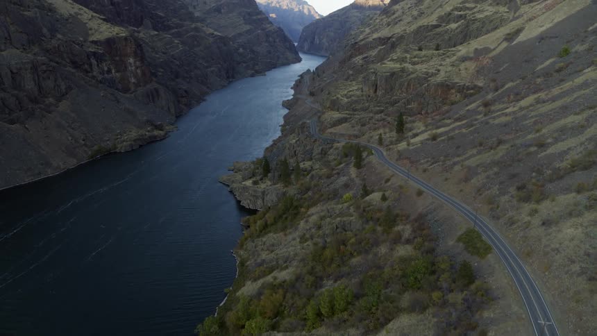 An empty road stretches along the side of a remote and rugged canyon next to a deep blue river