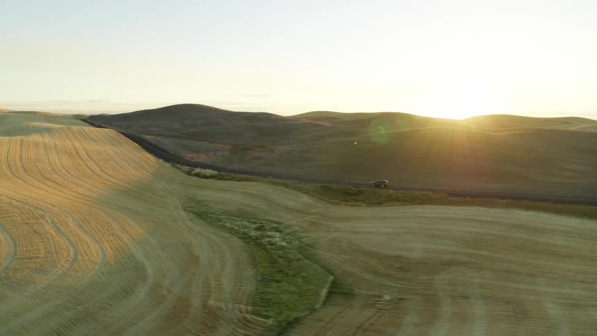 Following low behind a SUV driving through rolling farmland as the sun rises along the horizon