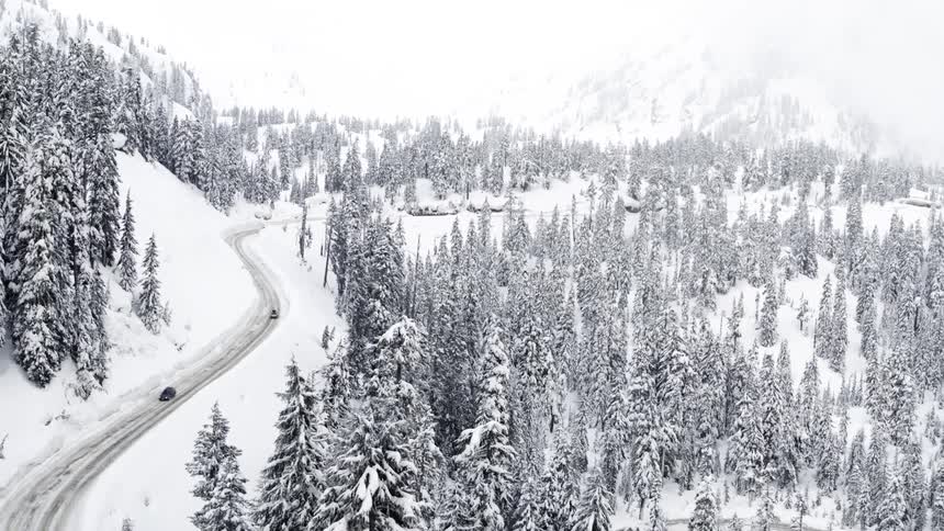 Cars travel carefully on a icy mountain road as it snows lightly