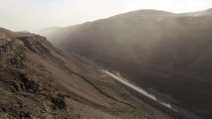 A car drives on an isolated rural road in a rugged canyon valley illuminated with dramatic light