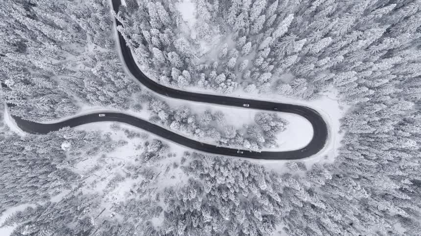 Top down descending twist over cars driving on a hairpin curve through a snow covered forest