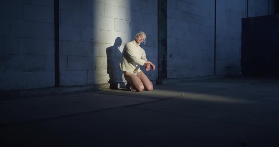 A woman without pants kneeling on the floor next to a cinderblock wall