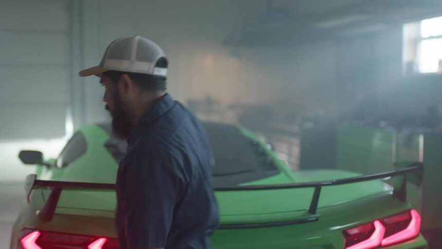 A man with a hat closing a car hood in a garage