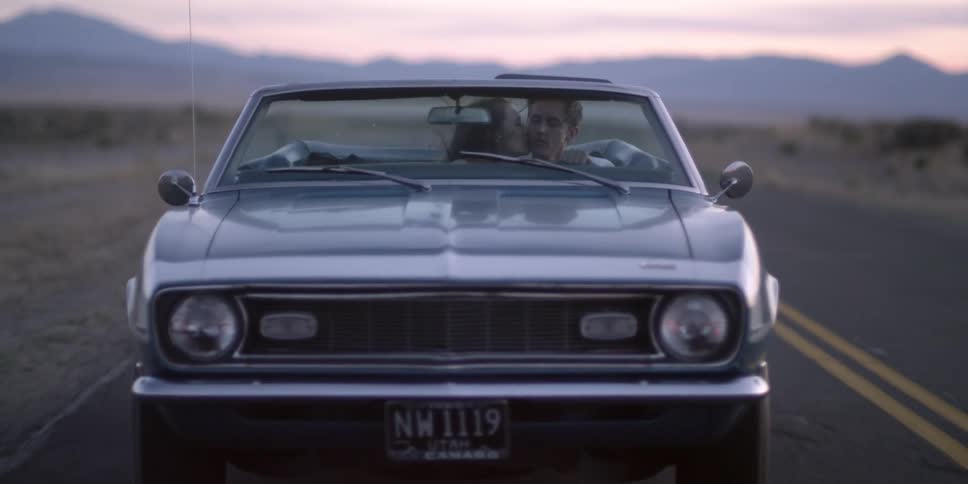 Woman leaning over kissing man while driving along the countryside in a convertible