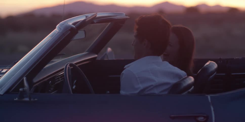A man and woman are sitting in a car at dusk