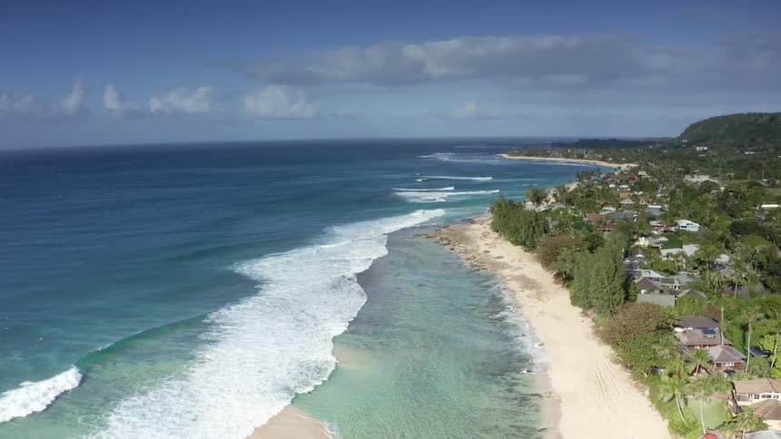 Waves roll across beach with trees and houses along the coastline
