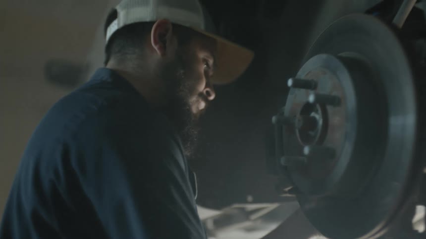 Car mechanic with a white cap and beard repairs a car at the garage