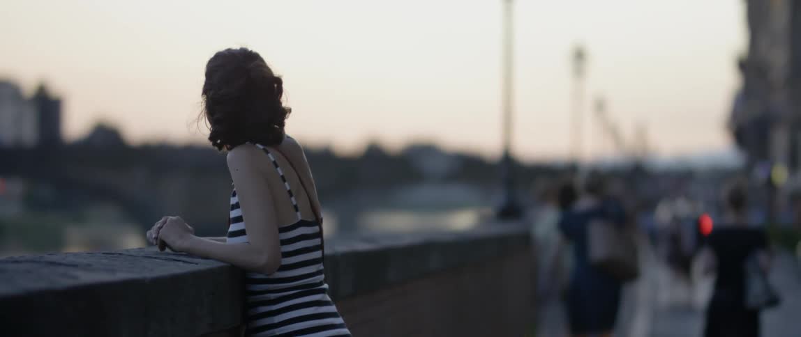 A woman stands on a bridge looking outward at dusk